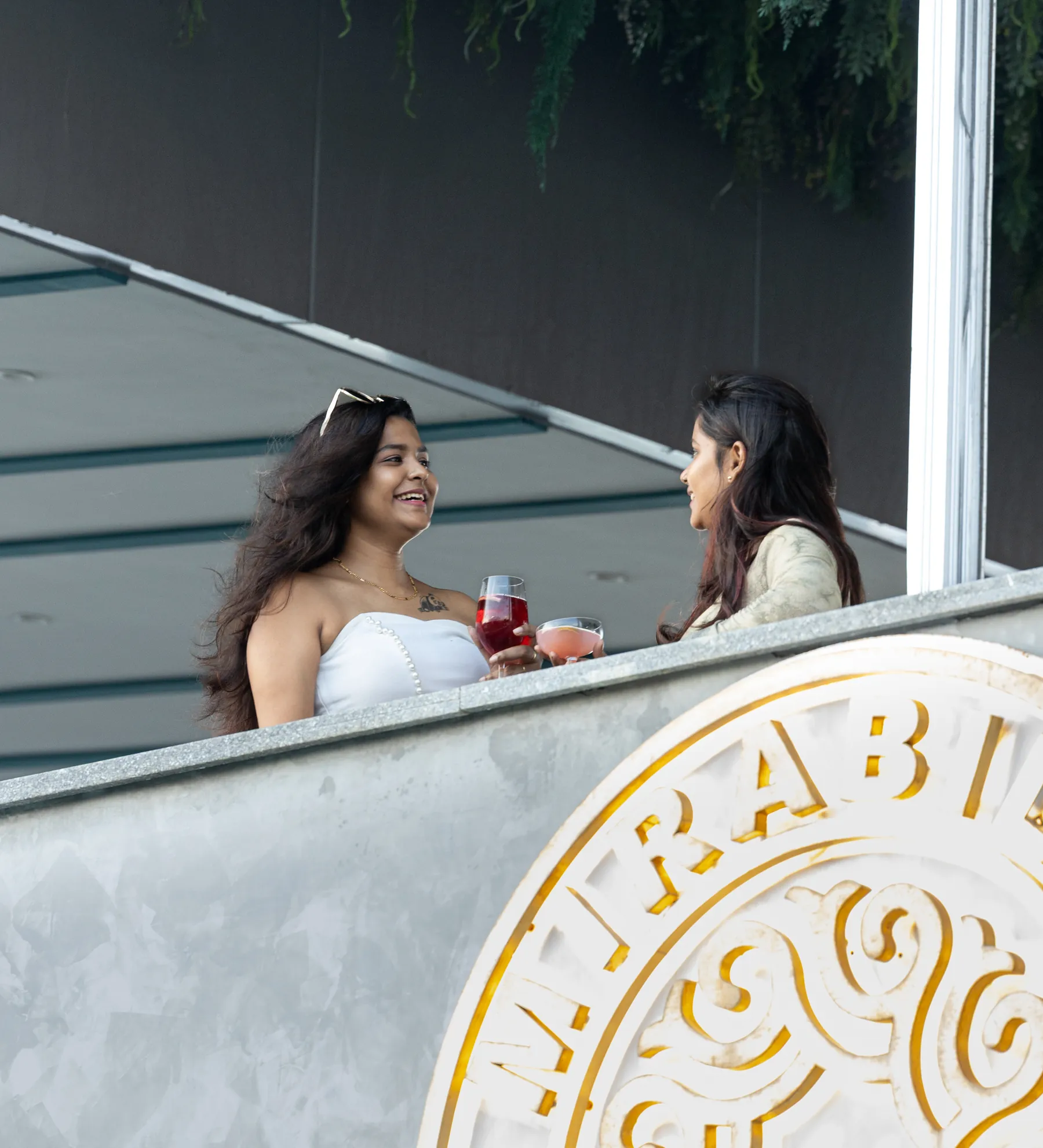 Two guests with drinks on the terrace, above the gold Mirabilis crest set into the parapet